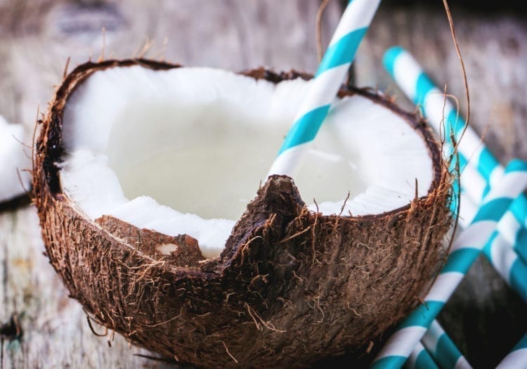 person drinking coconut milk directly from a coconut with a straw