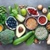 ¿Qué es la dieta integral basada en plantas? Selección de alimentos saludables: frutas, verduras, semillas, superalimentos, cereales con fondo gris.