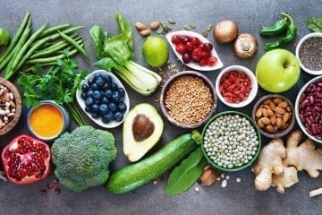 ¿Qué es la dieta integral basada en plantas? Selección de alimentos saludables: frutas, verduras, semillas, superalimentos, cereales con fondo gris.