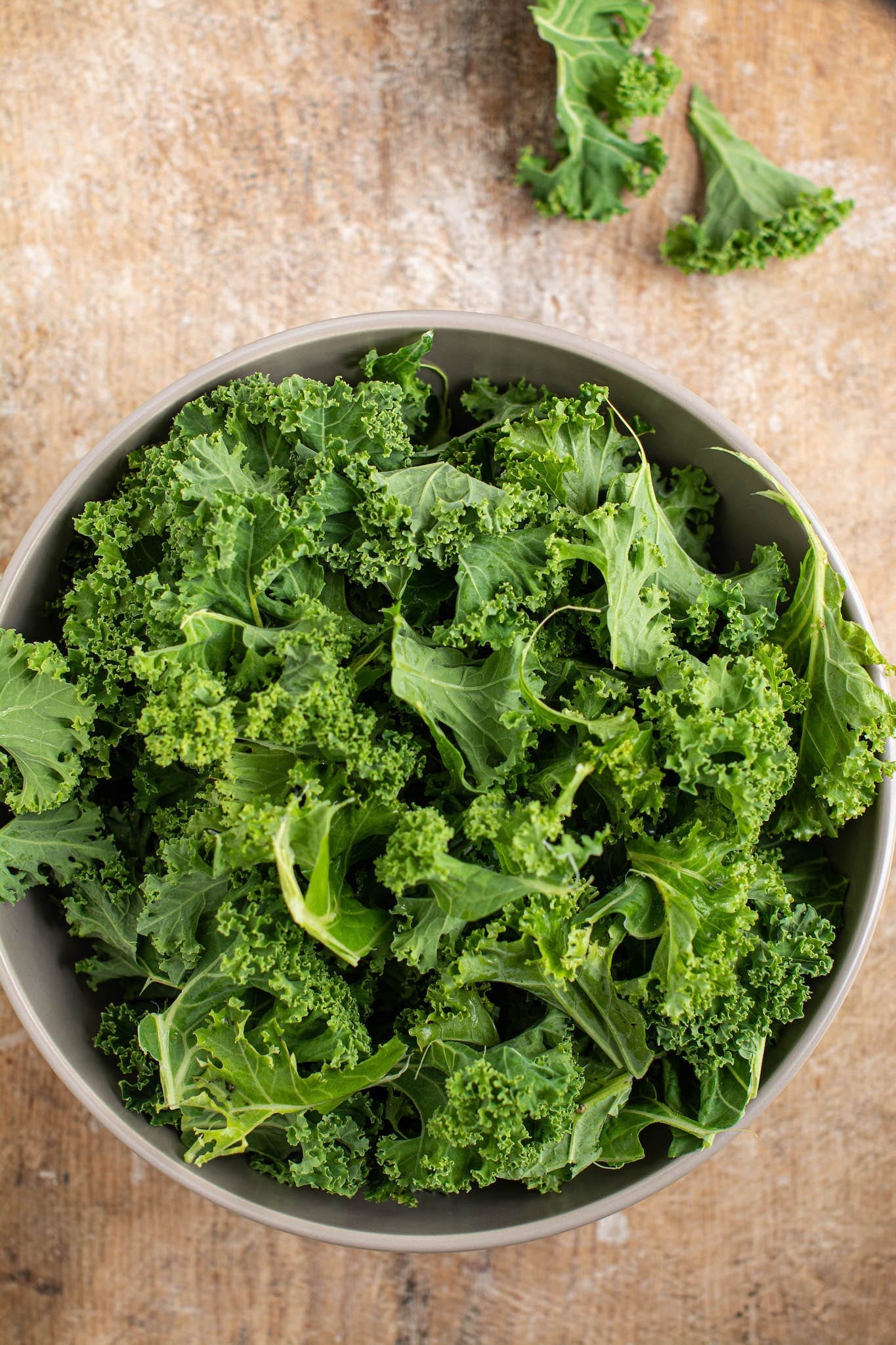 Fresh kale in a ceramic bowl on a wooden surface.